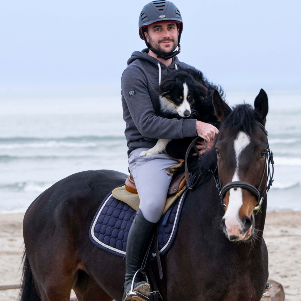 Moniteur d'équitation sur son cheval avec son chien à la plage.